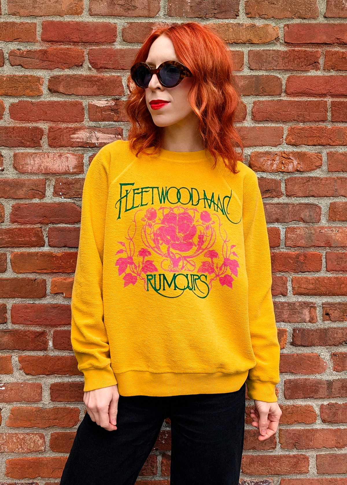 Fleetwood Mac Rumours sweatshirt with a reversed inside out textured look. Features a crew neckline, raglan sleeves, and ribbed cuffs, neckline, and hem. Golden Daze mustard colorway with flocked velvet writing in green and pink floral details. 100% French terry, made in the USA. Slouchy, relaxed fit 