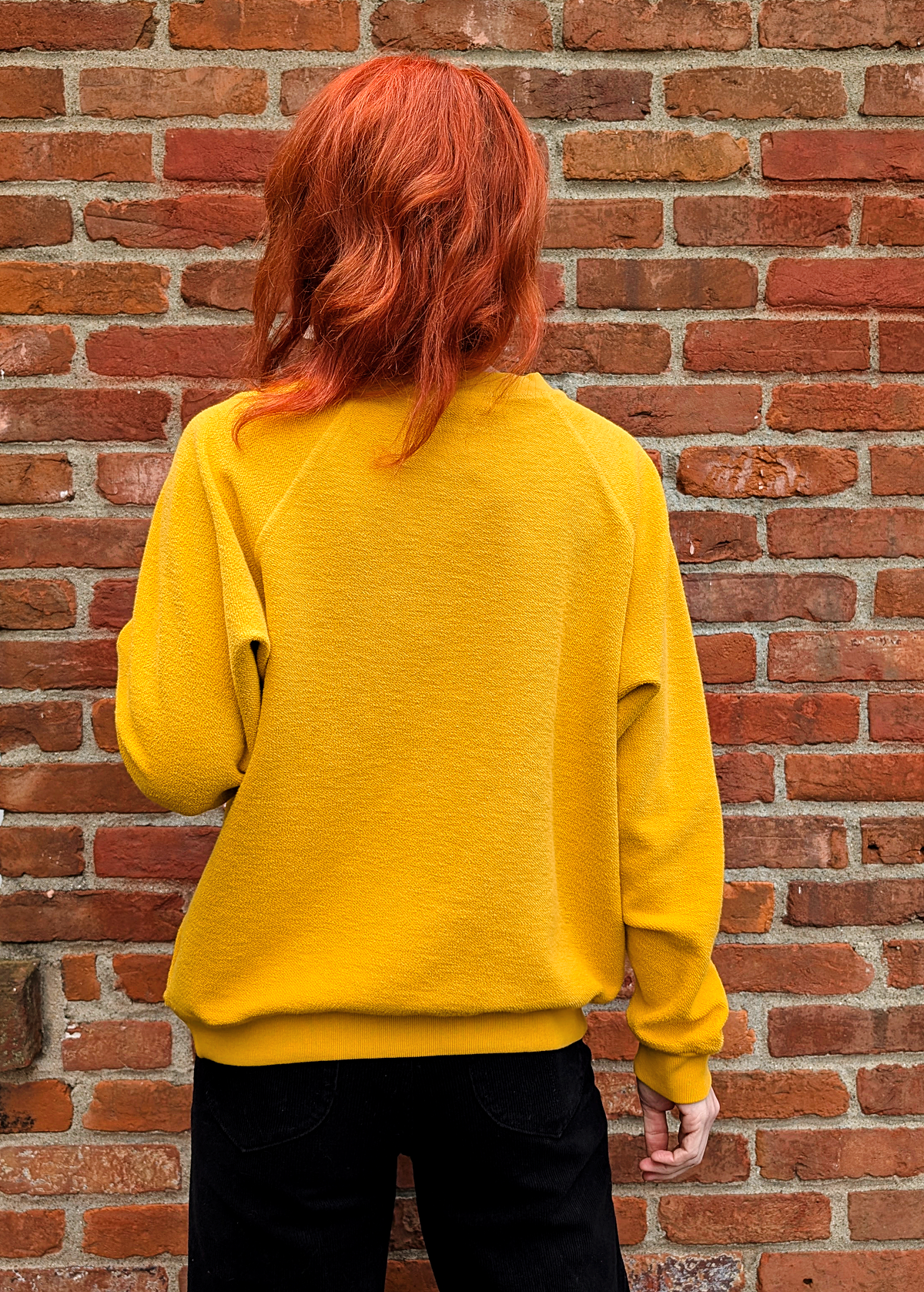 Back view of the Fleetwood Mac Rumours sweatshirt with a reversed inside out textured look. Features a crew neckline, raglan sleeves, and ribbed cuffs, neckline, and hem. Golden Daze mustard colorway with flocked velvet writing in green and pink floral details. 100% French terry, made in the USA