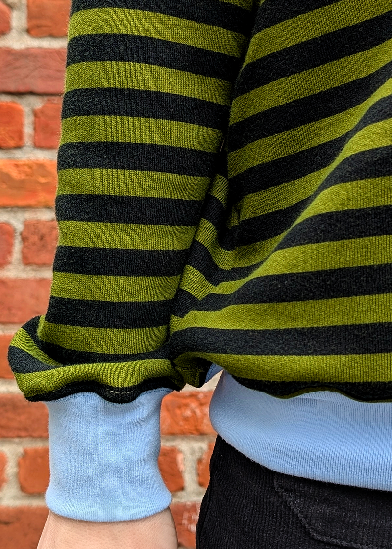 Details of the Olive green and black stripe raglan crew neck sweatshirt with ribbed sky blue cuffs, collar, and hem. Slouchy, relaxed fit. Made of 100% french Terry cotton